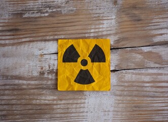 A yellow paper note with Radiation warning sign on it on a wooden surface. Close up.