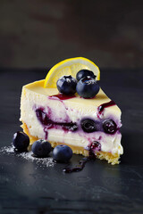 A slice of lemon blueberry cheesecake, showcasing its creamy texture and vibrant colors. The background is dark gray to highlight the colorful dessert, creating a visually appealing composition.