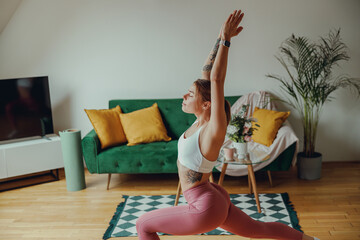 Woman is doing yoga in a living room with hardwood flooring and a green couch. Home workout concept