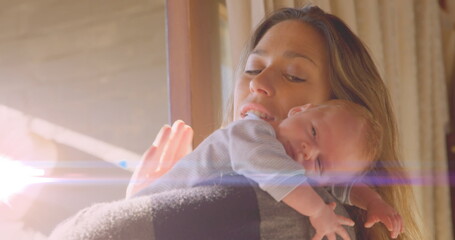 Image of glowing spots over happy caucasian mother with sleeping baby