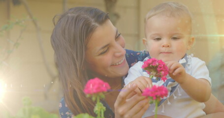 Image of glowing spots over happy caucasian mother with daughter holding flowers