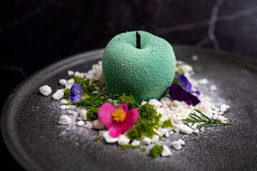 Innovative apple-shaped dessert, masterfully crafted, adorned with colorful petals and herbal...