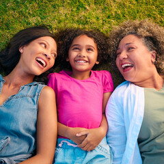 Looking Down On Three Generation Female Family Laughing And Lying On Grass Outdoors In Countryside - obrazy, fototapety, plakaty