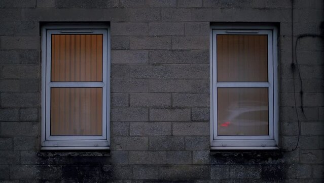 Two plastic frame windows on cinder block building facade, handheld shot