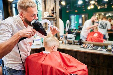 Competent barber styling fresh haircut. Back view of little boy getting new haircut. Male barber...