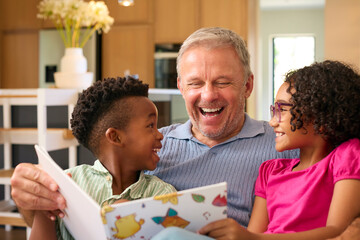Multi Racial Family With Grandfather Looking After Grandchildren At Home Reading A Story Together