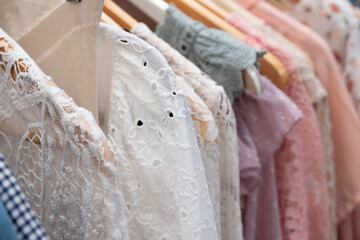 Cheap second-hand summer dresses with lace and fresh light colors hang on wooden hangers in a store. Narrow depth of field. Background image