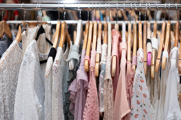 Cheap second-hand summer dresses finished with lace and in soft pastel shades hang on wooden hangers in a shop
