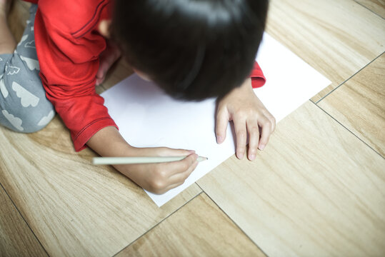 Little asian boy sitting on ground and drawing on paper