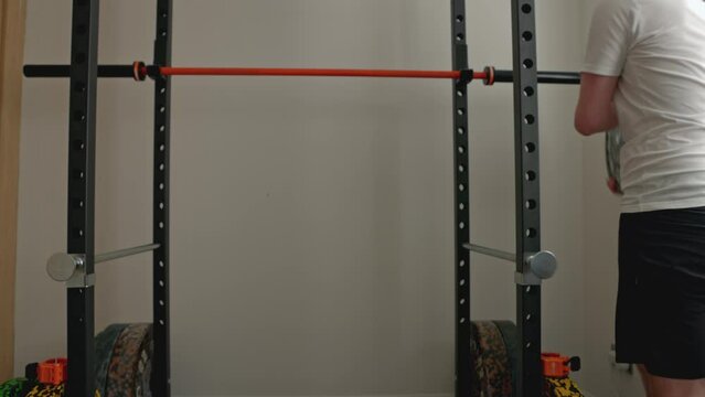 static shot of a man putting extra plates on a barbell in a squat rack