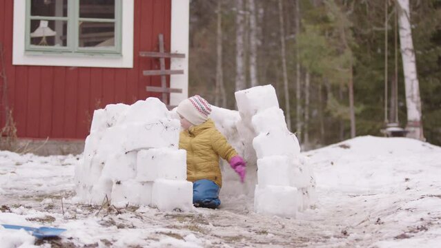 Boy in winter wear constructs igloo with snow blocks in yard, carefree childhood