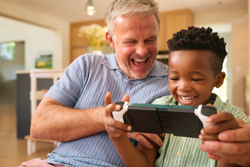 Multi Racial Family With Grandfather And Grandson Playing On Handheld Gaming Device Together - obrazy, fototapety, plakaty