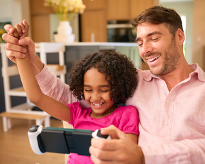 Multi Racial Family With Father And Daughter Playing On Handheld Gaming Device Together