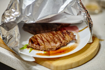 Grilled steak resting under aluminum foil before serving