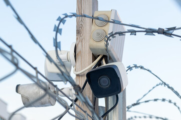 A camera is mounted on a pole next to a barbed wire fence