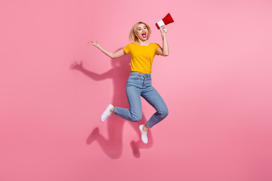 Full length photo of funky impressed woman wear yellow t-shirt jumping high yelling loud speaker empty space isolated pink color background