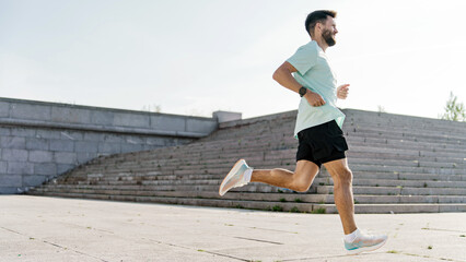 A bearded runner with a focused gaze propels forward in a dynamic stride along a vast urban...