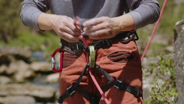 female athletic Rock climber preparing to climb rocks. woman climber checking rope knot on harness under cliff getting ready to climb. High quality 4k footage