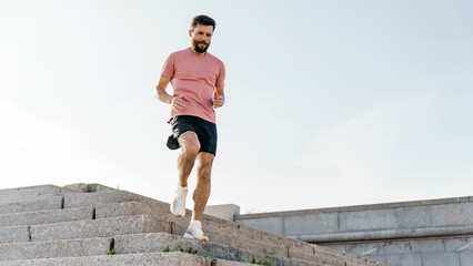 A focused man in a salmon-colored shirt ascends city stairs, a challenge against the sky's...