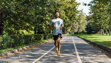 A focused jogger runs down a leaf-strewn park pathway, flanked by lush trees in the full bloom of...