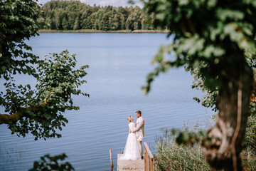 Valmiera, Latvia - August 10, 2023 - A couple in wedding attire embraces on a wooden dock by the...