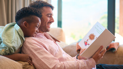 Multi Racial Family At Home With Father And Son Reading Book Together