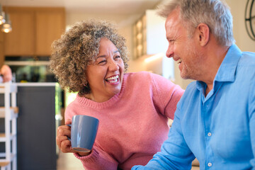 Loving Multi-Racial Mature Couple Sitting On Sofa At Home With Hot Drink Laughing And Talking