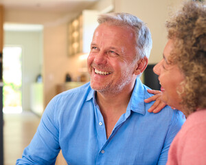 Loving Multi-Racial Mature Couple Sitting On Sofa At Home Laughing And Talking Together