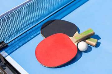 Two table tennis or ping pong rackets and ball on blue table with net