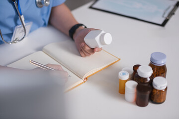 A doctor is writing in a notebook while holding a bottle of pills