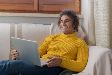 Smiling curly man working on laptop on sofa at home