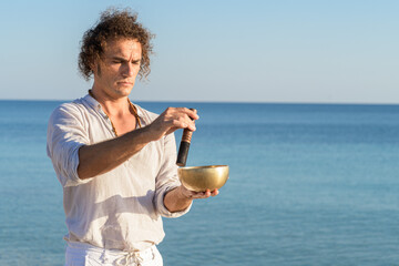 A man playing on a singing tibetian bowl for meditation on sea