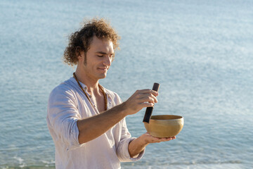 Smiling man playing on a singing tibetian bowl on the sea