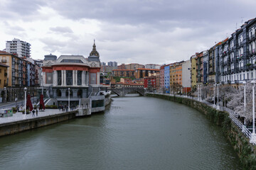 view of the old town with big river in center and colorful houses on cloudy day in bilbao