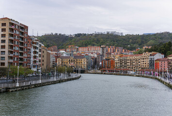 view of the old town with big river in center and colorful houses on cloudy day in bilbao