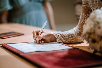 Valmiera, Latvia - August 10, 2023 - A person signing a document, lace sleeve, pen in hand, with a bouquet in the foreground. - obrazy, fototapety, plakaty
