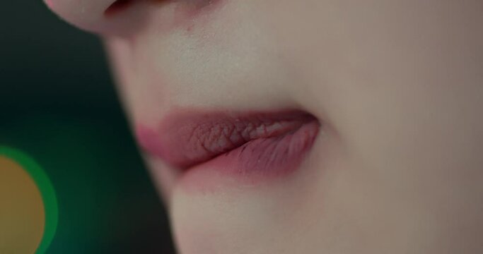 Female purses lips and bites sucking on them with bokeh lights behind, detailed shot