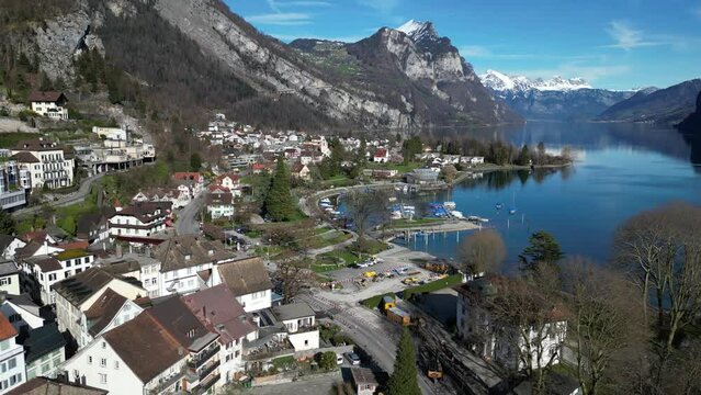 Drone clip showing white buildings in small lakeside village in Switzerland, with snowy mountains in the background