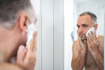 A man applies shaving foam to his face in the bathroom