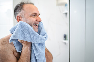 Portrait of a smiling man wiping his face with a towel after shaving