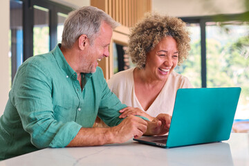 Smiling Multi-Racial Mature Couple At Home Looking At Laptop Together