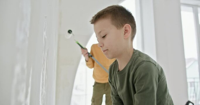 Two young boys actively participate in a home renovation project as they paint the walls of a new apartment. Captures the essence of family involvement and teamwork in DIY home improvement tasks.