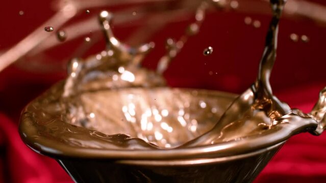 Ice cubes descend into a pool of golden liquid, causing it to ripple and dance beyond the confines of the bowl, a slow-motion scene with artsy connotations.