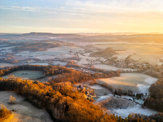 Golden sunrise bathing the rolling landscape of Bohemian Paradise with villages and fields in serene dawn light. Aerial drone photography.