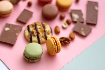 Pastel macarons, almond chocolate, peanut butter cookies and various nuts on bright pink background. Selective focus.