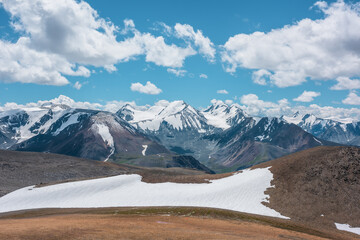 Aerial top view to stony pass and snow-white glacier on rocky hill in sunlight among high mountains in sunny day. Large colorful mountain range with snowy peaks in far away under clouds in blue sky. - 792784260