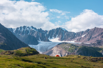 Colorful landscape with orange tent in alpine valley with view to big glacier tongue and large...