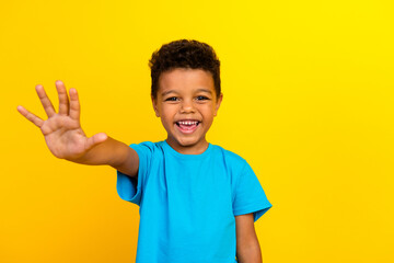 Photo of friendly cute positive child with curly hair dressed blue t-shirt give you highfive...