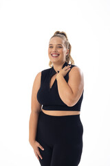 Caucasian young plus-size woman in black sportswear stands, smiling on white background