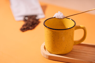 Yellow mug with a spoon of sugar and coffee beans.